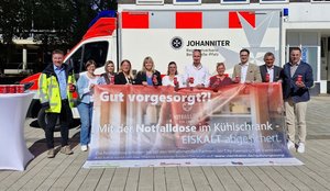 Gruppenfoto vor einem Einsatzfahrzeug der Johanniter: Vertreterinnen und Vertreter der Stadt Viernheim und beteiligter Partner halten rote Notfalldosen in die Kamera. Im Vordergrund präsentieren sie ein großes Banner der Aktion „Gut vorgesorgt?! – Mit der Notfalldose im Kühlschrank – EISKALT abgesichert.“