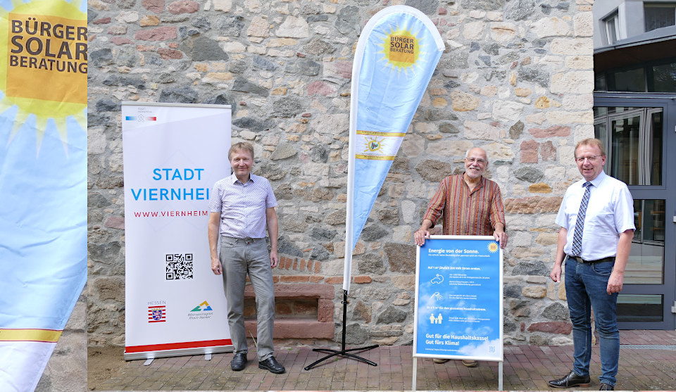 Brundtlandbeauftragter Philipp Granzow, Hans-Peter Dieter (BürgerSolarBeratung Weschnitztal) und Bürgermeister Matthias Baaß stehen vor Steinwand mit Plakaten zur BürgerSolarBeratung 