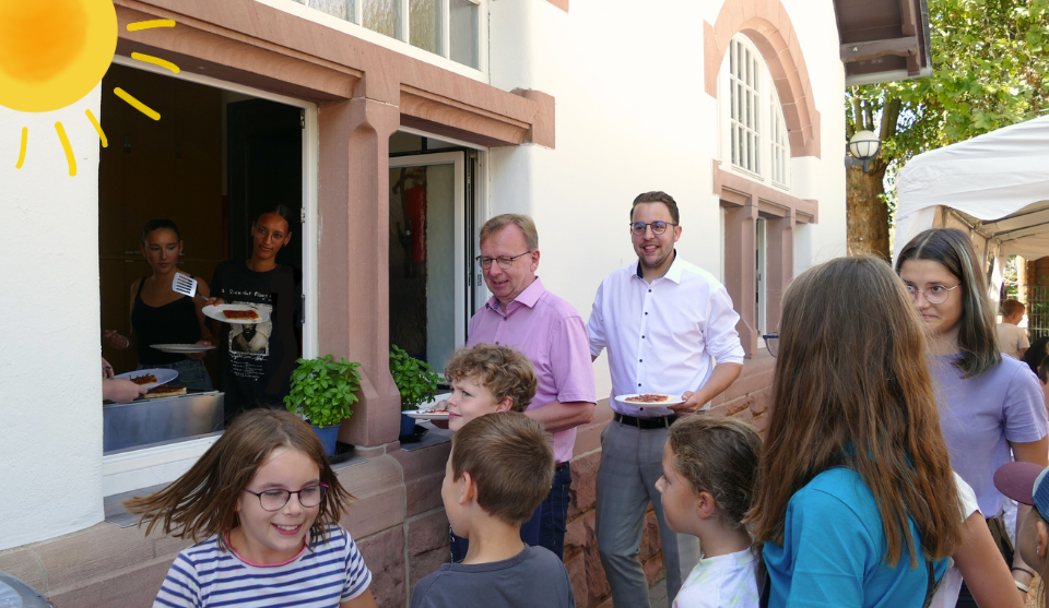 Bürgermeister Matthias Baaß und Erster Stadtrat Jörg Scheidel (hinten rechts) mit vielen Kindern an der Essensausgabe um sich Pizza zu holen.