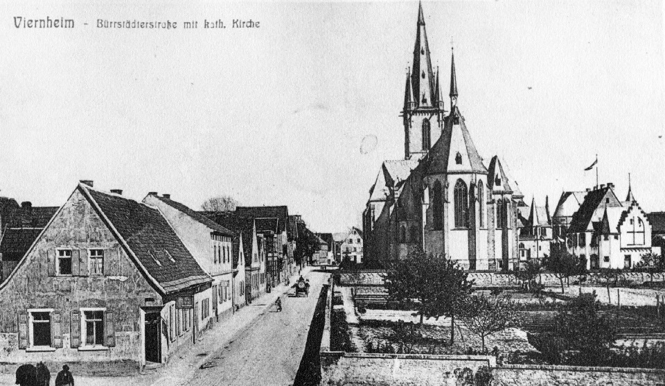 Das Foto zeigt Viernheim um 1900 mit der Bürrstädter Straße (heute Kettelerstraße), die St. Apostel-Kirche mit dem Ehatt'schen Garten davor sowie vorne links das Gasthaus „Zum Rebstock“. © Stadtarchiv Viernheim