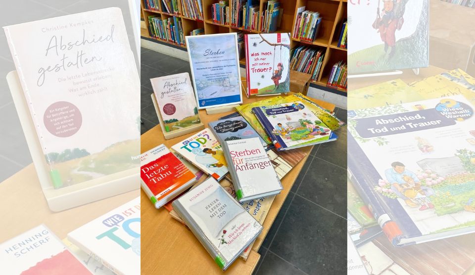 Auf einem Holztisch in der Stadtbibliothek Viernheim liegen und stehen verschiedene Sachbücher, Ratgeber und Kinderbücher zu Sterben, Tod, Trauer und Abschied. In der Mitte befindet sich ein gerahmter Informationsaufsteller zum Themenbüchertisch „Sterben – wenn das Leben leiser wird“. Im Hintergrund sind Bücherregale zu sehen.