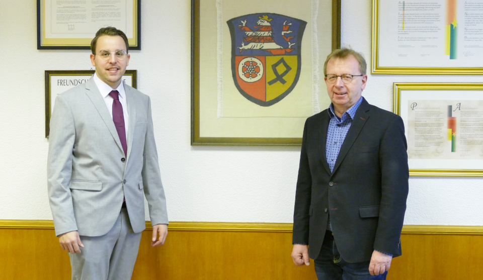 Jörg Scheidel und Bürgermeister Matthias Baaß stehen vor Wand mit Urkunden und Wappen der Stadt Viernheim