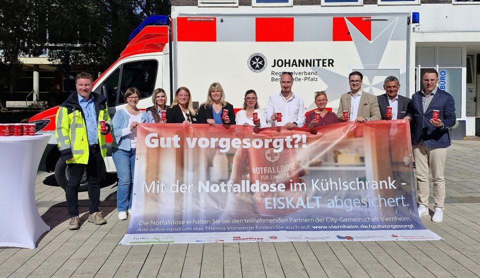 Gruppenfoto vor einem Einsatzfahrzeug der Johanniter: Vertreterinnen und Vertreter der Stadt Viernheim und beteiligter Partner halten rote Notfalldosen in die Kamera. Im Vordergrund präsentieren sie ein großes Banner der Aktion „Gut vorgesorgt?! – Mit der Notfalldose im Kühlschrank – EISKALT abgesichert.“