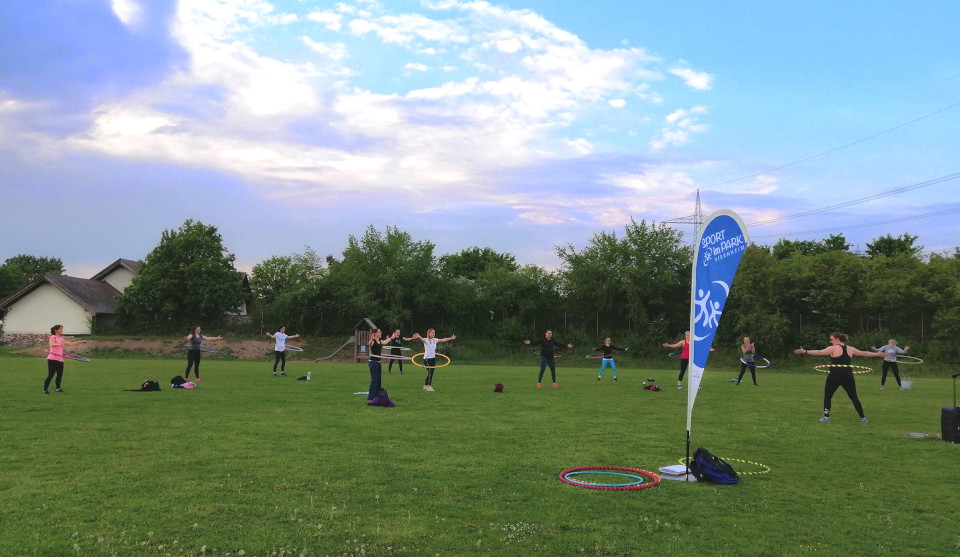 Menschen trainieren auf Rasenfläche mit Hula Hoop Reifen