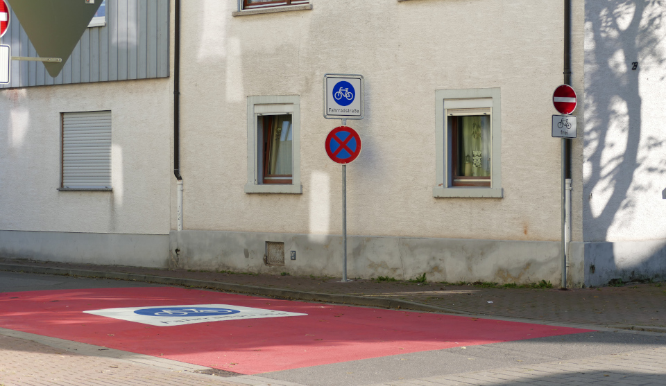 Einfahrt in Fahrradstraße Schild rechts weißes Fahrrad auf blauem Kreis und roter Streifen auf Bodenbelag mit Fahrradsymbolschild