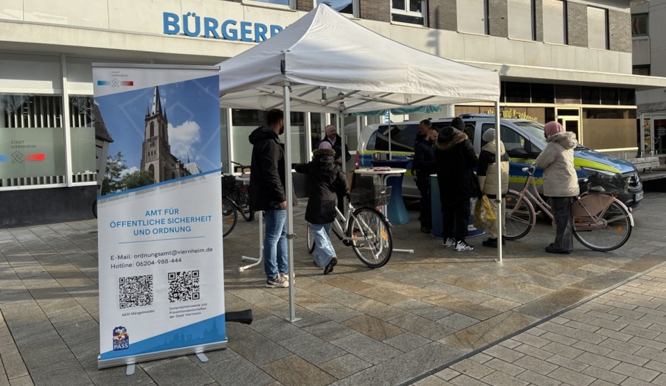 kleines weißes Zelt mit Schild Amt für öffentliche Sicherheit und Ordnung und Menschen die ihr Fahrrad an den Stand schieben
