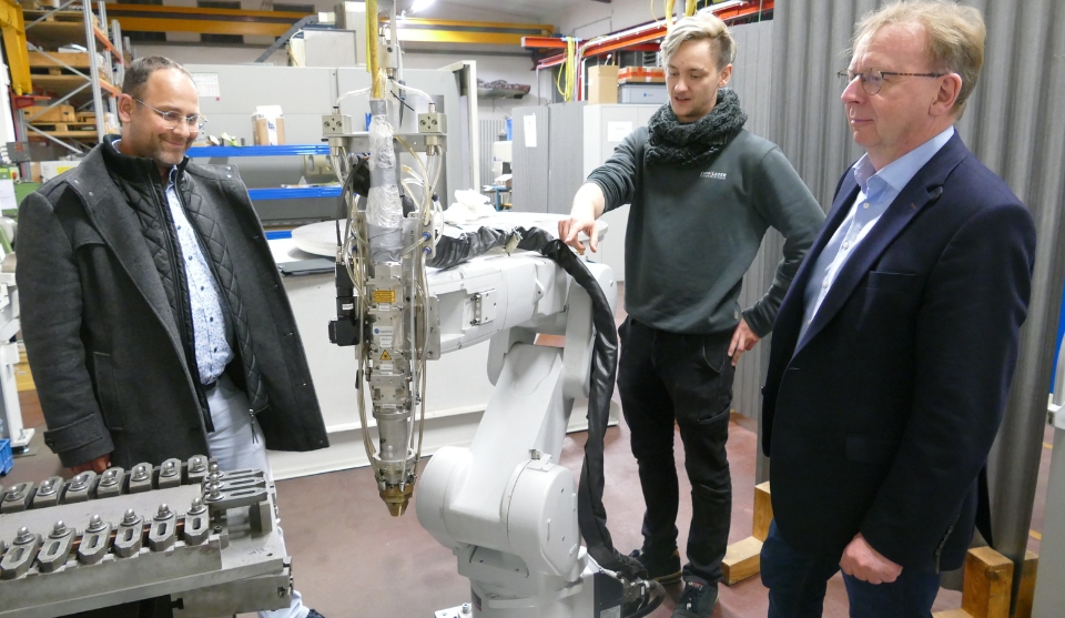 Florian Kiss (Mitte) zeigt Bürgermeister Matthias Baaß (rechts) und Wirtschaftsförderer Alexander Schwarz das Verfahren mittels Roboter mit Laserschweißkopf auf.