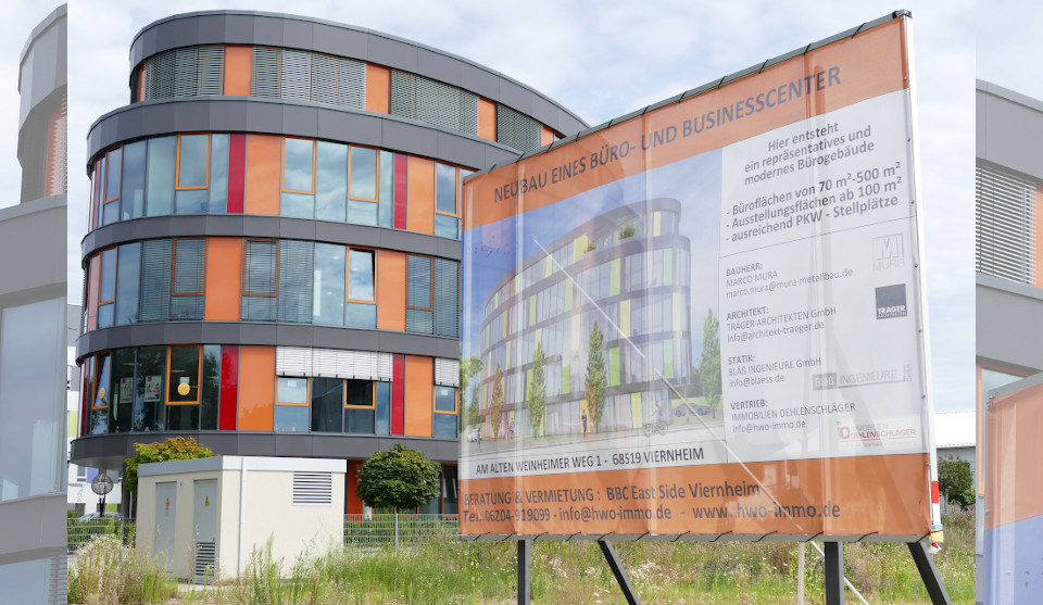Bürogebäude in Ellipsenform, davor Bauschild mit Werbung für Bauprojekt Ellipse II