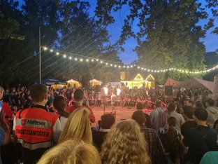 Menschen stehen um Arena, in der Mitte ein Mann mit zwei Feuerfackeln