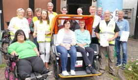 Zwei Frauen und viele Menschen dahinter sitzen auf einer orangenen Rikscha.