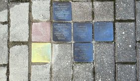 Mehrere Stolpersteine sind zwischen grauen Pflastersteinen in den Boden eingelassen. Die Gedenksteine erinnern mit Namen und Angaben zu Flucht, Deportation und Ermordung an Mitglieder der Familie Schindler. Der linke Stein glänzt und scheint neu zu sein. Er erinnert an Frieda Horn, geborene Schindler.