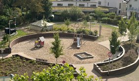 lick von oben auf den Spitalplatz mit einem begrünten Spielplatz. Zu sehen sind unter anderem eine Rutsche, ein Sandkasten, ein kleines Spielhaus, Schaukeln, Sitzbänke sowie zahlreiche Bäume und Beete. Im Hintergrund stehen Wohnhäuser.