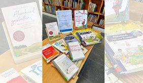 Auf einem Holztisch in der Stadtbibliothek Viernheim liegen und stehen verschiedene Sachbücher, Ratgeber und Kinderbücher zu Sterben, Tod, Trauer und Abschied. In der Mitte befindet sich ein gerahmter Informationsaufsteller zum Themenbüchertisch „Sterben – wenn das Leben leiser wird“. Im Hintergrund sind Bücherregale zu sehen.