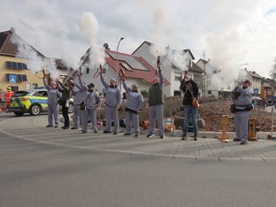 Zehn Personen in schwarz/weiß gestreifter Kleidung schießen in die Luft