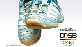 Zu sehen ist ein Paar Sportschuhe in Weiß und Hellblau, die vor einem hellgrauen Hintergrund frei aufgehängt oder schwebend dargestellt sind. Die Schuhe sind übereinander angeordnet, sodass die Profilsohlen teilweise sichtbar sind. Gebrauchsspuren an Material und Sohlen deuten darauf hin, dass die Schuhe regelmäßig genutzt wurden. Rechts im Bild befinden sich mehrere Logos und Schriftzüge. Zu lesen ist: „WIR SIND SPORTDEUTSCHLAND“ sowie das Logo des DOSB (Deutscher Olympischer Sportbund). Darunter sind die fünf olympischen Ringe in Blau, Gelb, Schwarz, Grün und Rot abgebildet. Links unten steht die Internetadresse „sportdeutschland.de“. Die Gestaltung ist schlicht und konzentriert sich auf die Sportschuhe als Symbol für Bewegung, sportliche Aktivität und Fitness. Das Motiv eignet sich als Illustration für Themen wie Sportabzeichen, Breitensport oder sportliche Veranstaltungen.
