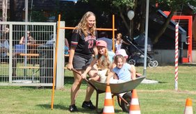 Frau schiebt Kinder in einer Schubkarre.