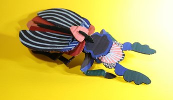 Aus Karton und Farbe wurde ein Insekt gebastelt. Auf gelben Untergrund. 