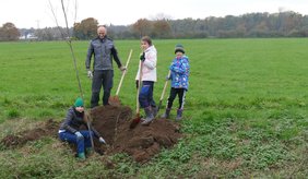 Kinder und Jugendliche die an einem Graben Bäume pflanzen
