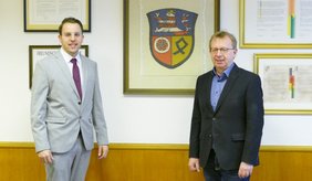 Offizielle Begrüßung des neuen Ersten Stadtrats im Magistratszimmer der Stadt Viernheim: (v. l.) Jörg Scheidel und Bürgermeister Matthias Baaß. ©Stadt Viernheim Jörg Scheidel und Bürgermeister Matthias Baaß stehen vor Wand mit Urkunden und Wappen der Stadt Viernheim