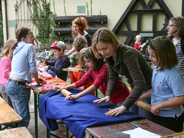 Ferienaktionen für Kinder im Alter von 6 - 10 Jahren Kinder und Erwachsene stehen an Tisch und arbeiten gemeinsam
