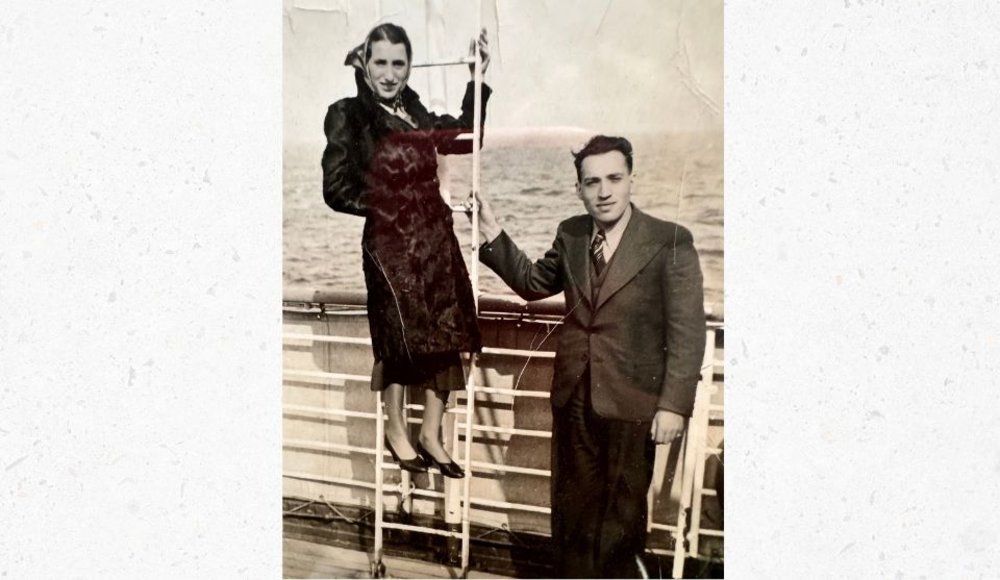 Historische Schwarz-Weiß-Aufnahme einer und eines Mannes auf dem Deck eines Schiffes. Die Frau in dunklem Mantel und Kopftuch steht auf den unteren Sprossen einer Leiter. Neben ihr steht ein Mann im dunklen Anzug mit Krawatte und hält sich an der Leiter fest. Beide blicken in die Kamera. Im Hintergrund sind die Reling des Schiffes und das Meer zu sehen.