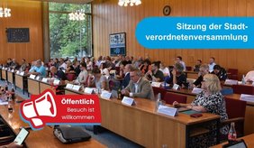 Blick in einen gut besuchten Sitzungssaal mit zahlreichen Personen an langen Tischreihen. Eingeblendet sind die Hinweise „Sitzung der Stadtverordnetenversammlung“ und „Öffentlich – Besuch ist willkommen“.