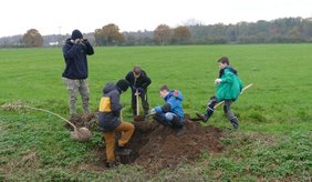 Kinder und Jugendliche die an einem Graben Bäume pflanzen