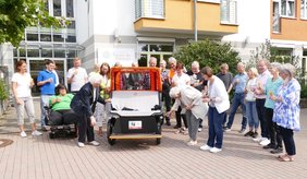 Zwei Frauen und viele Menschen dahinter taufen eine orangenen Rikscha mit einem Glas Sekt.