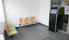 Der Wartebereich inklusive Terminal, an dem sich die Bürgerinnen und Bürger für ihren vorab vereinbarten Termin anmelden können. ©Stadt Viernheim Sitzbänke mit grünem Polster und ein schwarzes Terminal