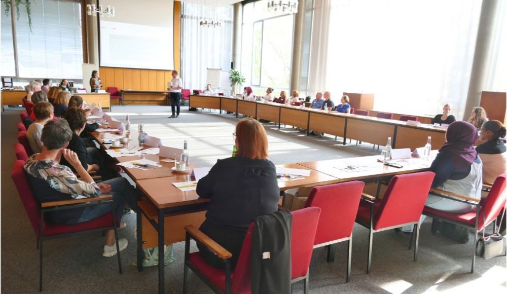 Blick in einen hellen Sitzungssaal mit großen Fenstern und U-förmig angeordneten Tischen. Rund 30 Personen sitzen auf roten Stühlen, hören den Vortragenden zu und tauschen sich aus. Auf den Tischen liegen Unterlagen, Notizblöcke und Wasserflaschen. Das Treffen findet im Rahmen des achten Runden Tisches „Im Alter gut versorgt in Viernheim“ statt.
