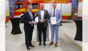 Innenminister Roman Poseck (Bildmitte) übergibt die Förderbescheide an Bürgermeister Matthias Baaß (links) und Ersten Stadtrat Jörg Scheidel.