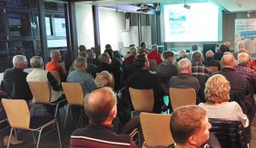 Zahlreiche interessierte Bürgerinnen und Bürger kamen zu dem Vortrag in die Kulturscheune. ©Stadt Viernheim Personen sitzen auf Stühlen und schauen auf Präsentation