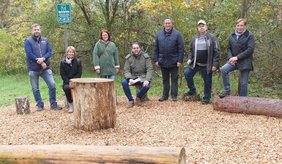 Präsentieren den neuen Walderlebnispfad: Sieben Personen sitzen oder stehen im Wald