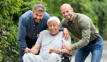 Ein älterer Mann im Rollstuhl zwischen zwei jüngeren Männern lachend