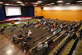 Bürgermeister Baaß informiert im Rahmen einer Präsentation die rund 100 Gäste ©Stadt Viernheim Personen sitzen auf Stühlen vor Präsentation