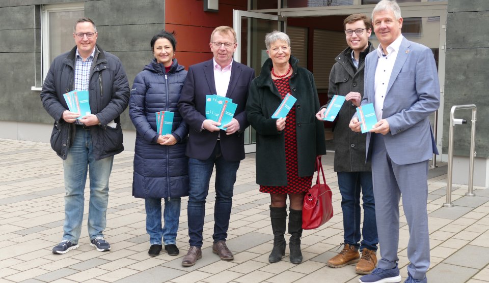 Sechs Personen stehen vor einer Eingangstür und halten die Programmheftchen in der Hand