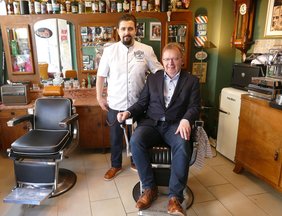 Ein Besuch wie in einer anderen Zeit: Bürgermeister Matthias Baaß nimmt im historischen Barbierstuhl von 1910 Platz, während Inhaber Lorenzo Mazzuca seine Barberia vorstellt.