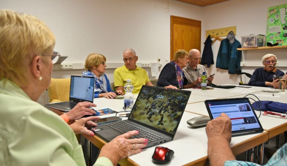 Mehrere Seniorinnen und Senioren sitzen gemeinsam an einem Tisch und nutzen Laptops, Tablets und Smartphones. Beim DigitalTREFF der SBS 55+ beschäftigen sie sich gemeinsam mit digitalen Anwendungen und Fragen rund um die Nutzung von Internet und mobilen Geräten.