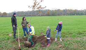 Kinder und Jugendliche die an einem Graben Bäume pflanzen